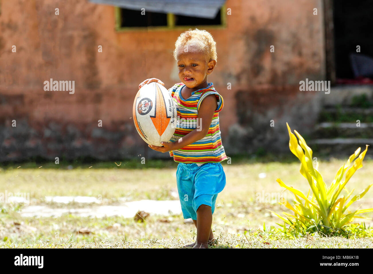 Kleiner Junge spielt mit Rugby-Ball in Lavena Dorf, Insel Taveuni, Fidschi. Rugby ist als der Nationalsport des Landes Stockfoto