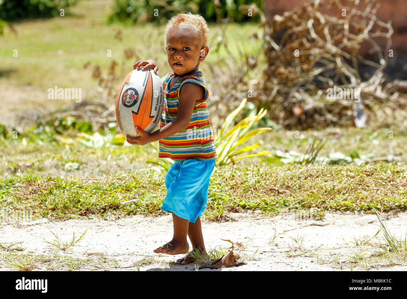 Kleiner Junge spielt mit Rugby-Ball in Lavena Dorf, Insel Taveuni, Fidschi. Rugby ist als der Nationalsport des Landes Stockfoto
