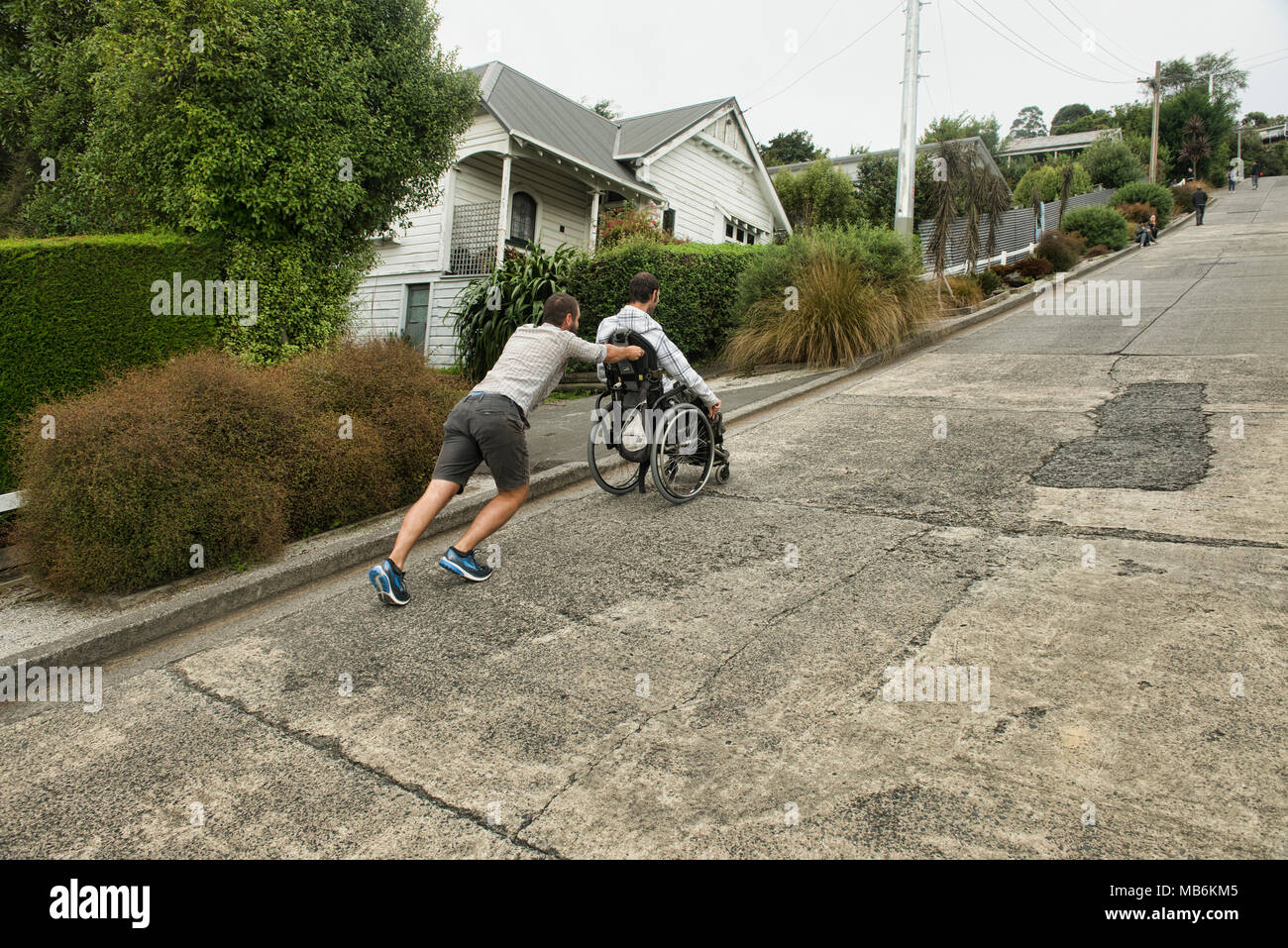 Freund seinen Kumpel Drücken in einem Rollstuhl bis Baldwin Street, der steilsten Strasse der Welt, Dunedin, Neuseeland Stockfoto