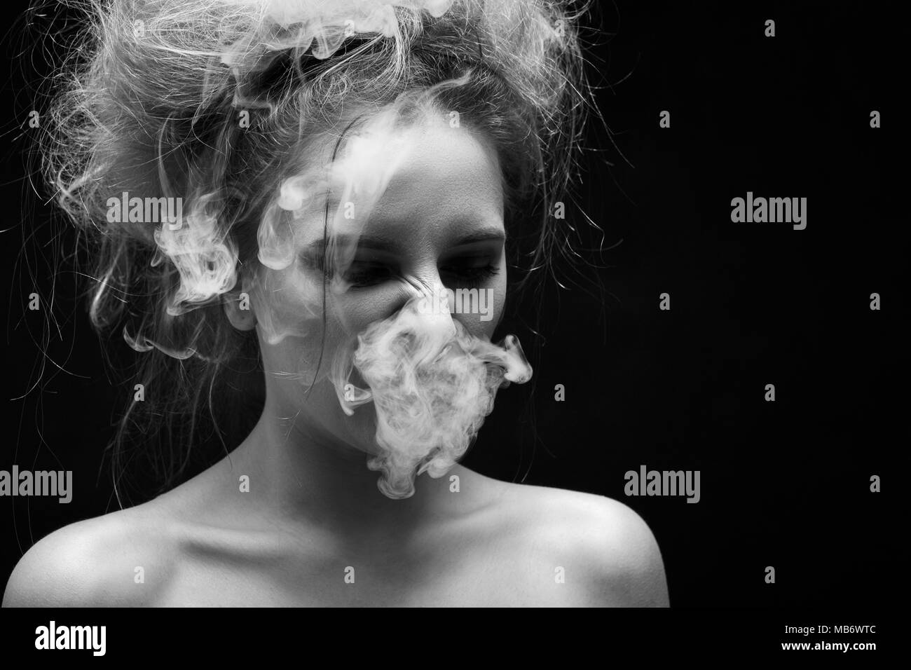 Mädchen Husten von Tabakrauch auf schwarzem Hintergrund, Monochrom Stockfoto