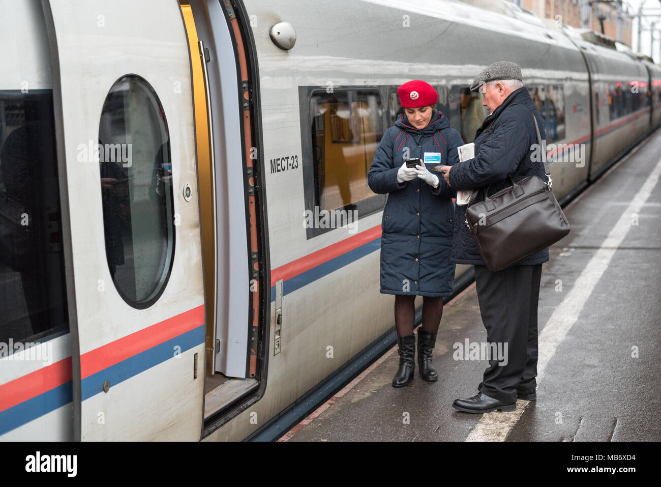 Zugbegleiter (rote Baskenmütze, Jacke) von sapsan Zug Kontrollen im Passagier mit elektronischen Gerät Bahnhof Moskau, Sankt Petersburg, Russland Stockfoto