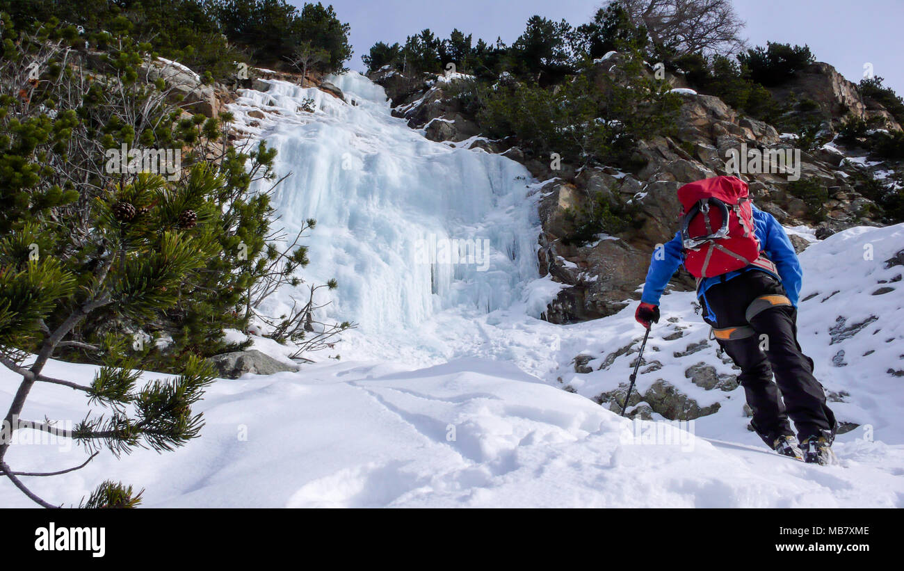 Männliche Eiskletterer in einer blauen Jacke und roter Rucksack Ansätze ein Eis fallen an einem schönen Wintertag und bereitet sie zu klettern Stockfoto