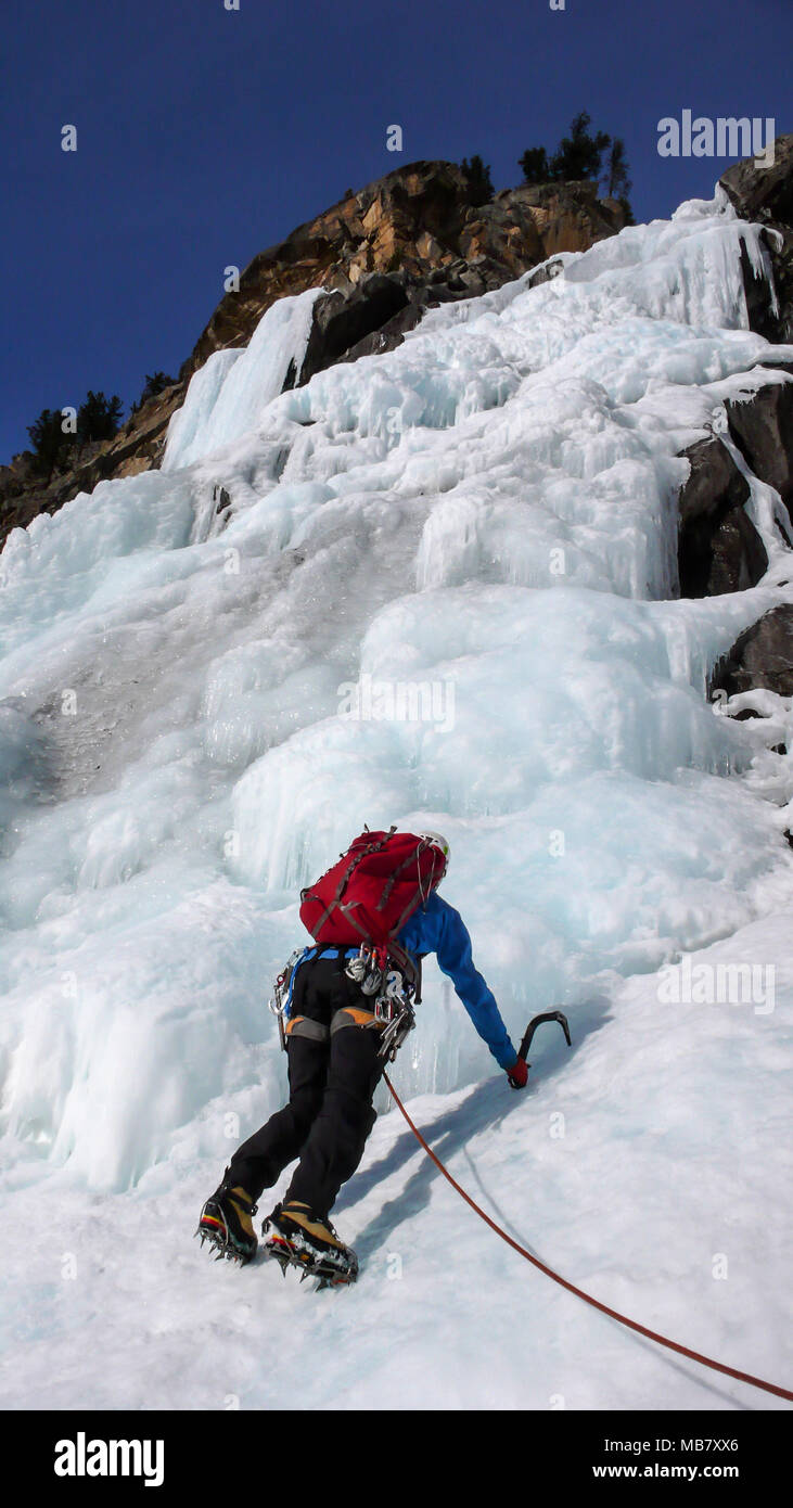 Männliche Eiskletterer in einer blauen Jacke auf einem wunderschönen gefrorenen Wasserfall Klettern in den Alpen, im tiefen Winter Stockfoto