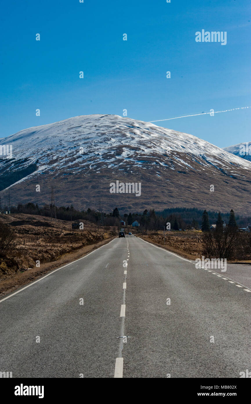 Eine einsame, leere Straße in den schottischen Highlands mit schneebedeckten Bergen in der Nähe der historischen Stätte von Glencoe, einer der großen Festplatten in Europa. Stockfoto