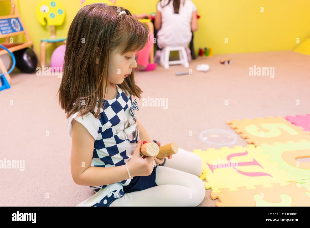 Cute Pre-school Mädchen an einer bunten puzzle Spielteppich suchen Stockfoto