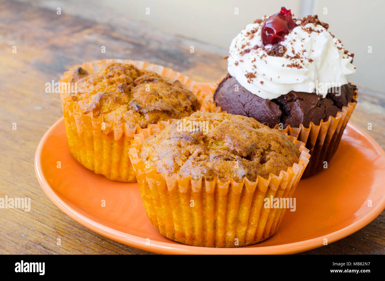 Orange Platte mit zwei Zitronen muffin Muffins und eine Schokolade mit Sahne und Kirschen auf einem alten Holztisch Stockfoto