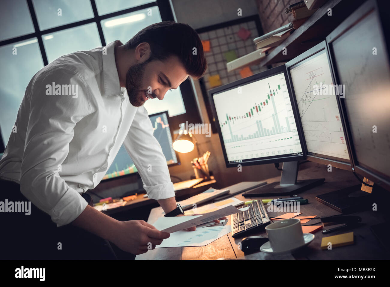 Junger bärtiger Mann Händler im Büro in der Nähe von Table bei Dokumente lächelt fröhlich Wachstum suchen Stockfoto