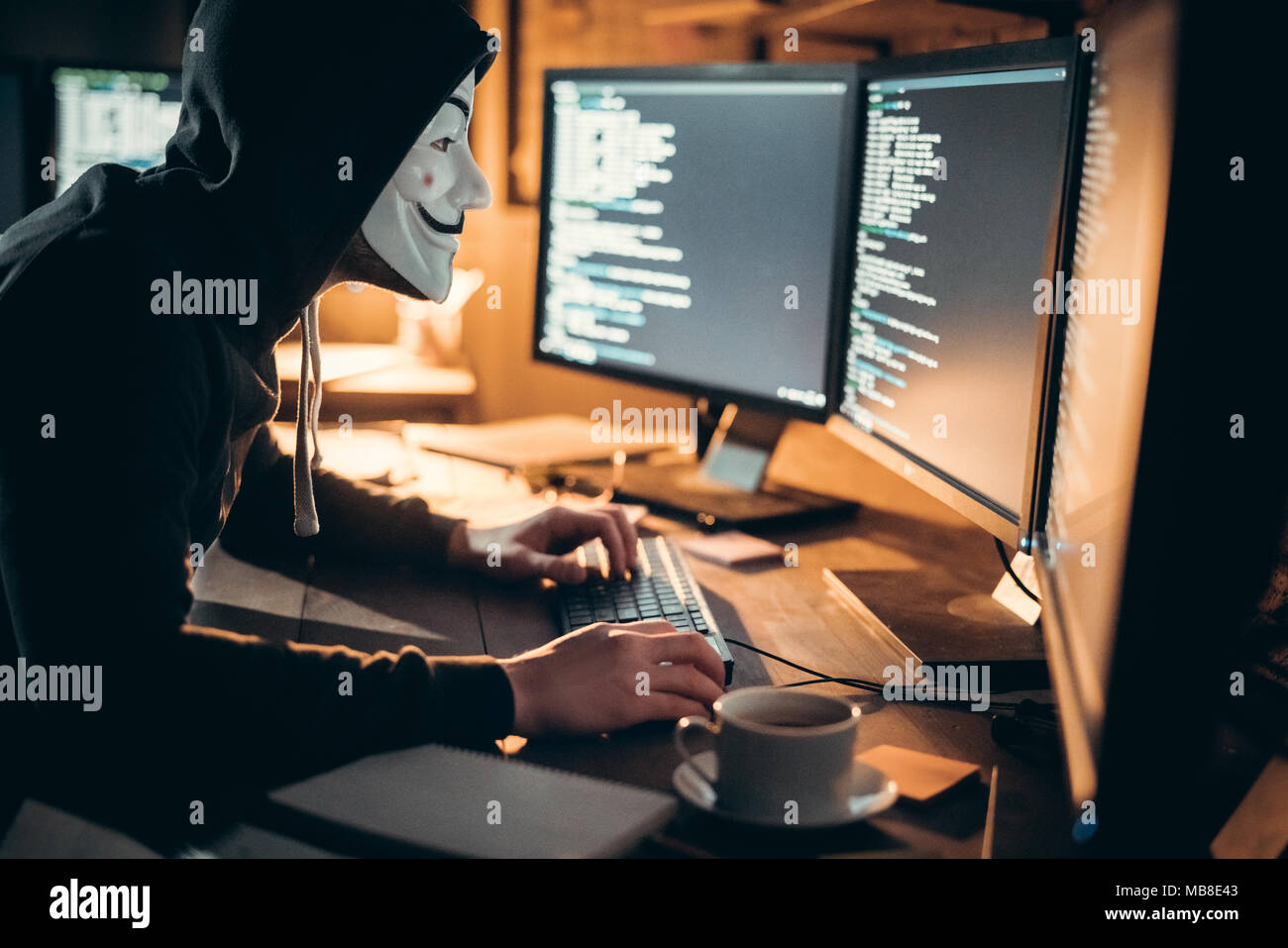 Junger Mann finanzielle Hacker im Büro sitzen am Tisch tragen Maske Informationen zu stehlen Stockfoto