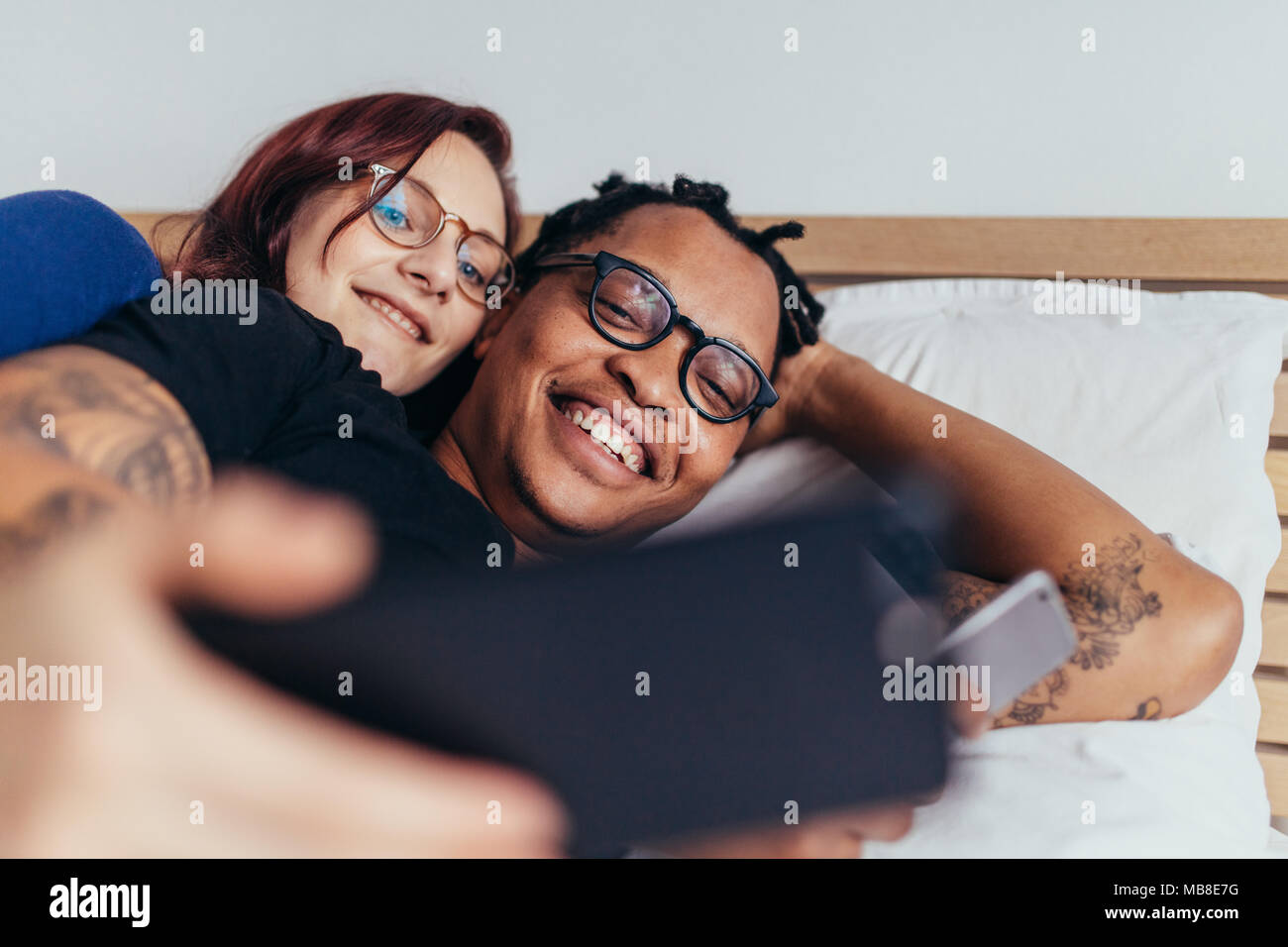 Fröhliche gemischtrassiges Paar zusammen im Bett liegen und unter selfie. Lächeln, Mann und Frau, die selfie mit Handy. Stockfoto