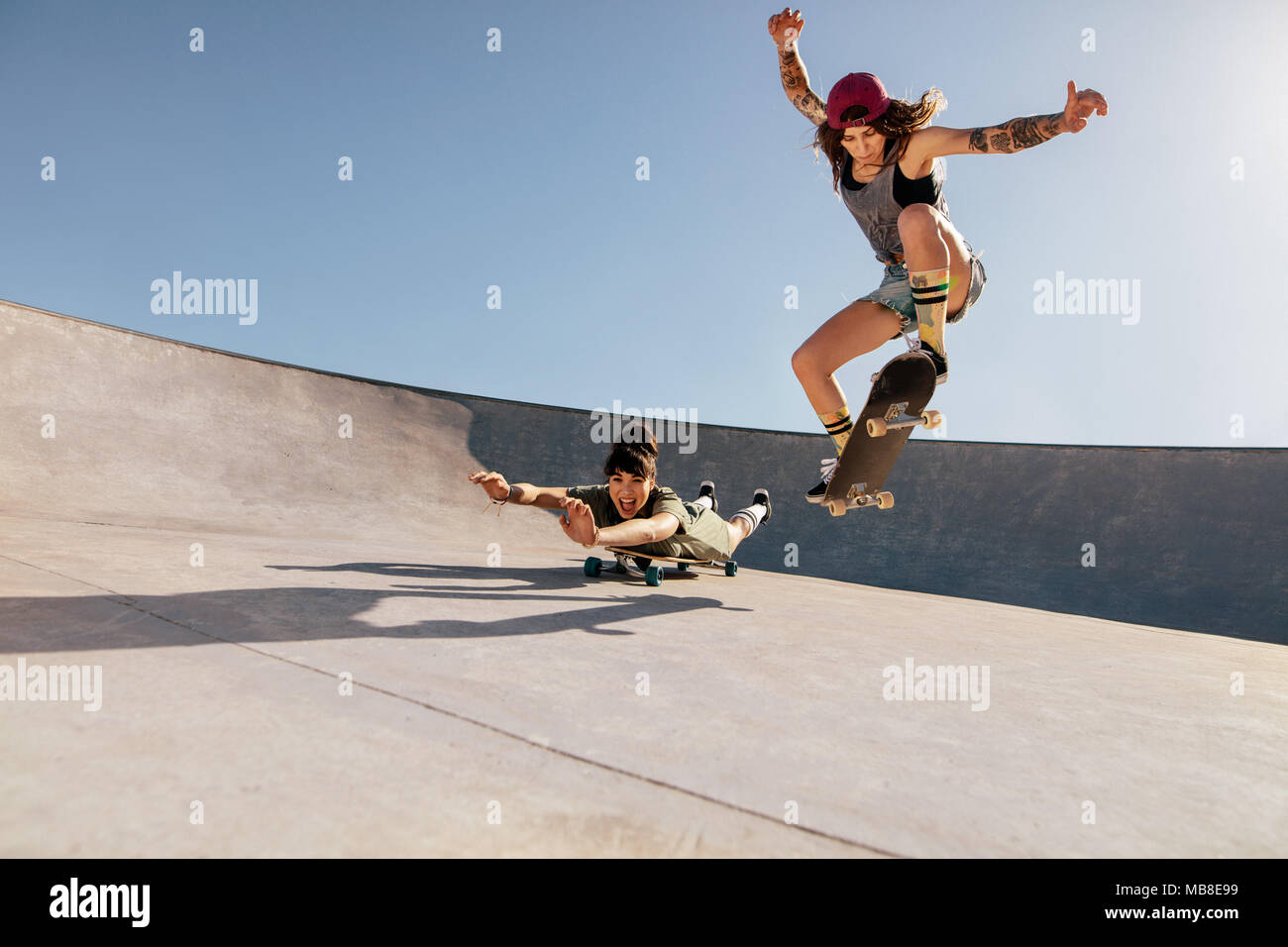 Zwei Frauen, die Stunts auf Skateboards bei Skate Park. Weibliche Freunde üben Skateboarding im Freien. Stockfoto