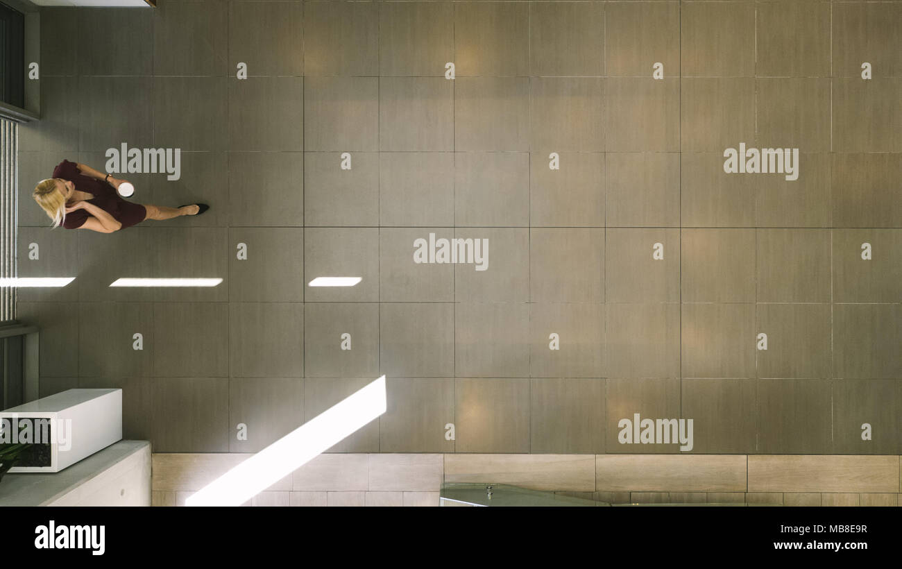 Blick von oben auf eine Geschäftsfrau eingabe Büro Flur mit Kaffee und Gespräch am Handy. Blick von oben auf die geschäftsfrau im Bürogebäude Lobby. Stockfoto