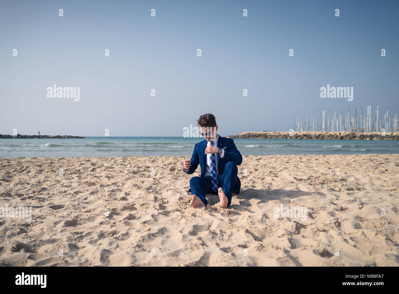Lustig Manager im eleganten Anzug ist entspannt am Strand. Stilvolle Kerl sitzt im Sand und haben Zeit zum Ausruhen Stockfoto