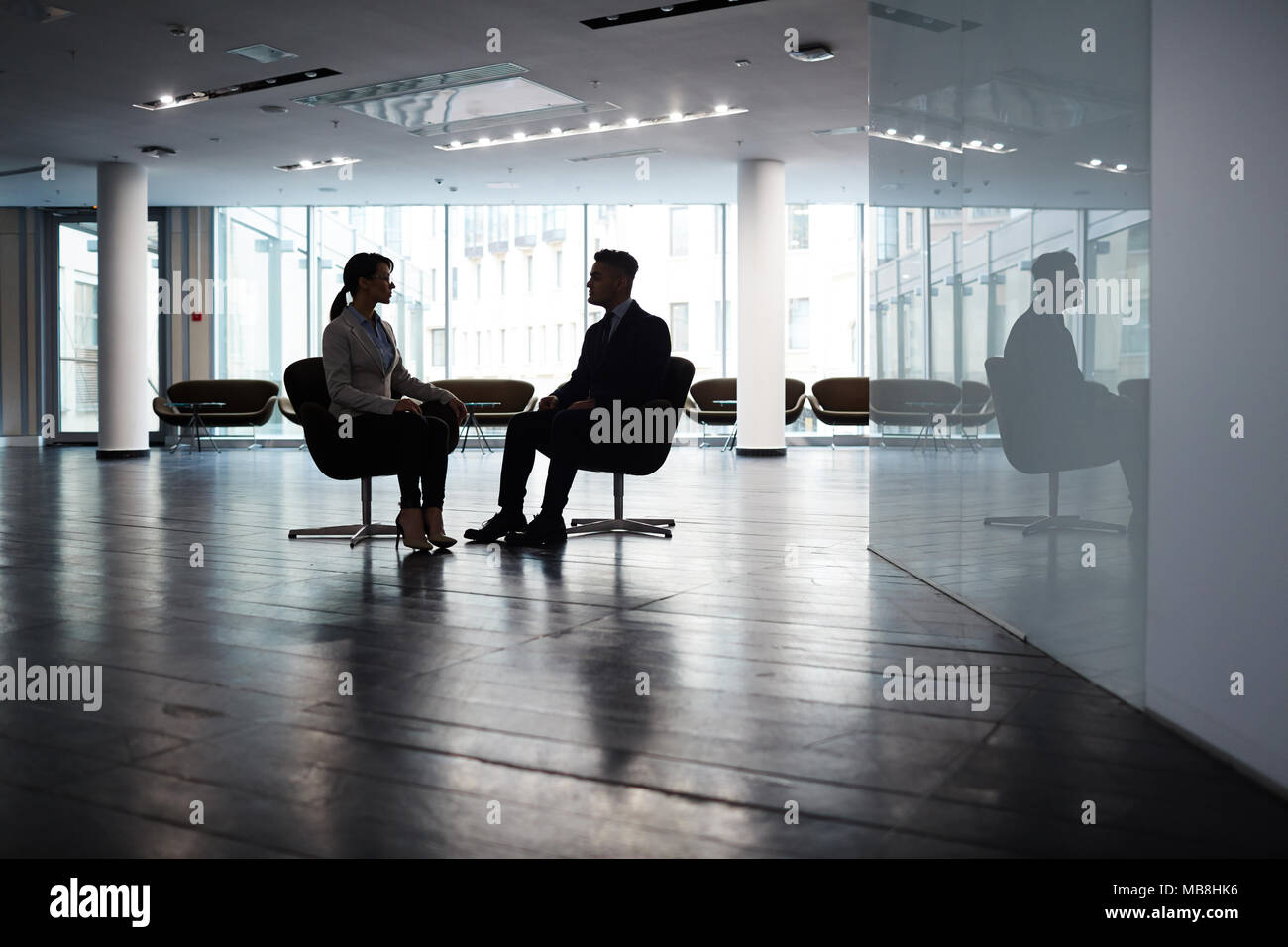 Selbstbewussten jungen Manager sitzen gegenüber ihren männlichen Partner beim Brainstorming über gemeinsame Projekt, Interieur des geräumigen dim Office Lobby im Hintergrund Stockfoto