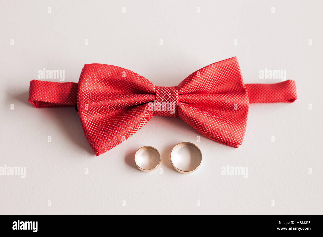 Nahaufnahme Blick von oben auf die elegante stilvolle Rot männlich bowtie und zwei goldene Ringe isoliert. Vorbereitung für die Hochzeit Konzept. Horizontale Farbfotografie. Stockfoto