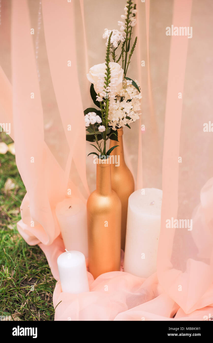 Details zu schöne festliche Dekoration für Hochzeit. Detailansicht der gemalten goldenen Wein Flaschen mit Blumen und weißen Kerzen in Pastelltönen fab Stockfoto