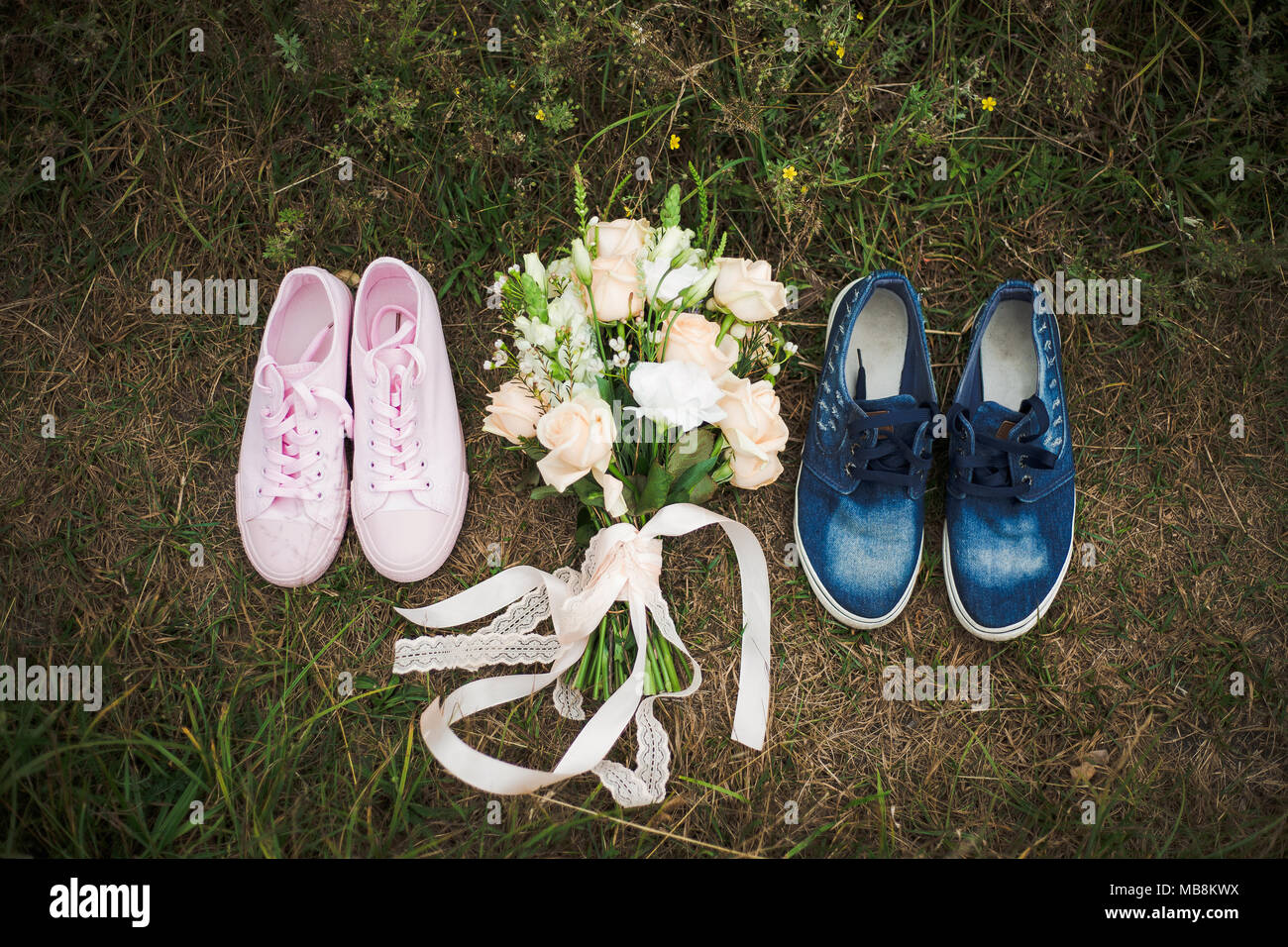 Nahaufnahme Blick von oben auf die weiblichen Trainer Schuhe Rosa und Blau männlichen Trainer Schuhe am Boden steht im Freien. Festliche pastell Blumenstrauß zwischen Pai Stockfoto