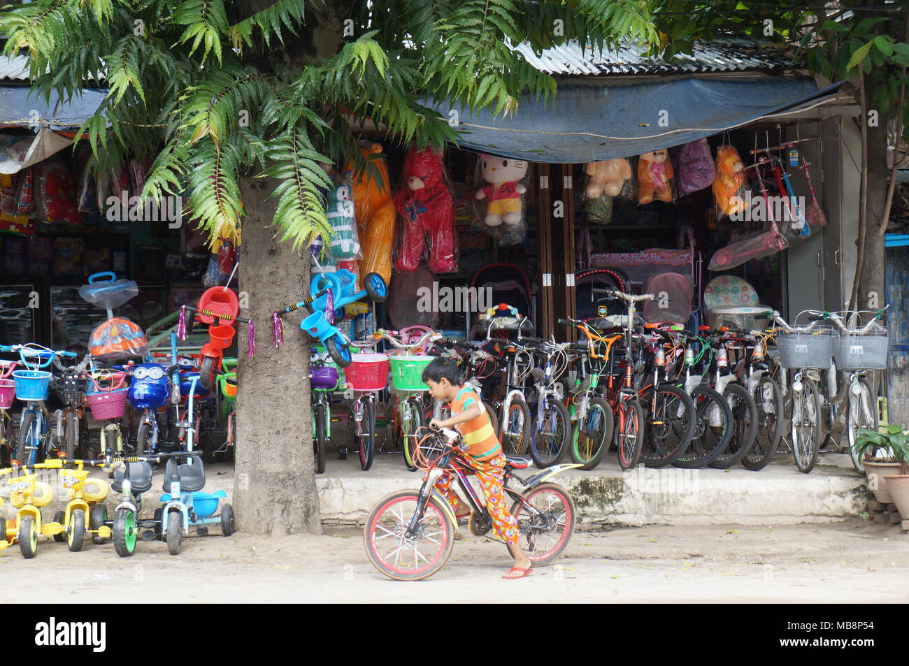 Burmesischer Junge, der auf seinem Fahrrad vor einem Fahrradladen für Kinder, Nyaung U Market, Bagan, Myanmar, reitet Stockfoto