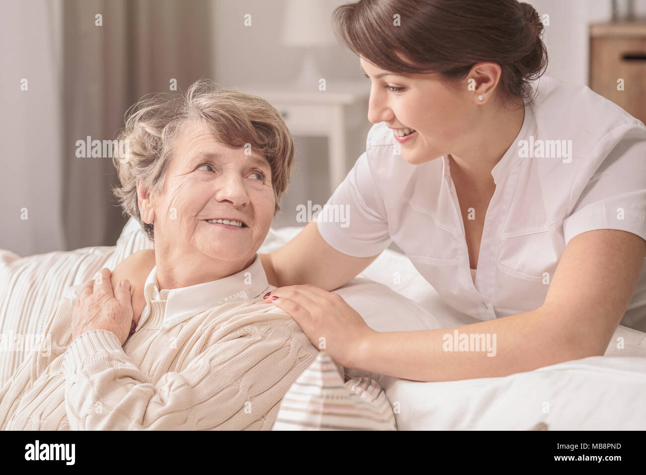 Hilfsbereit, junge, hübsche Krankenschwester unterstützt eine ältere nette Dame, die mit Alzheimer in einem Seniorenheim Stockfoto