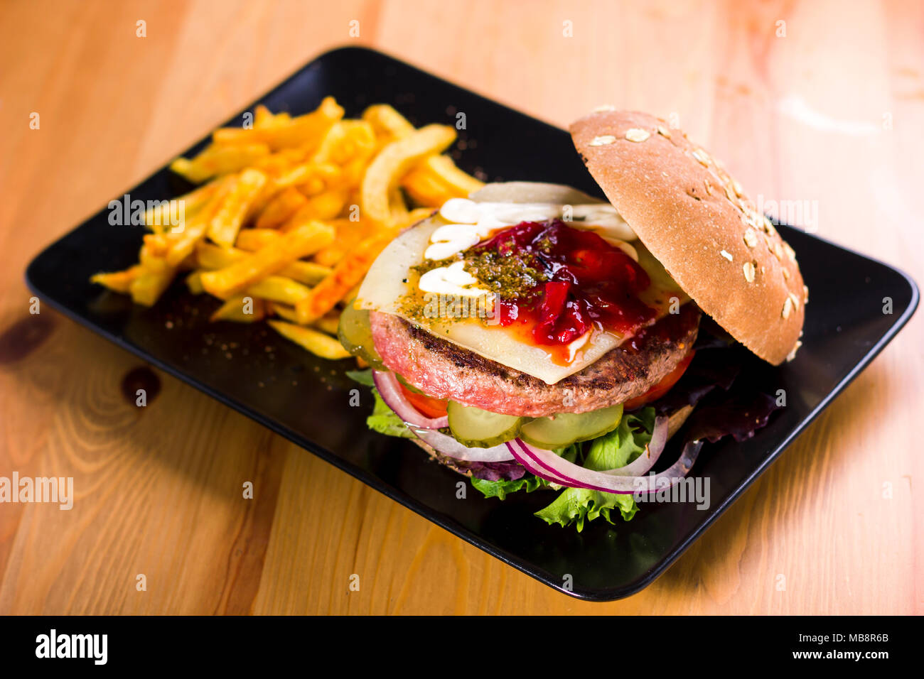 Hamburger mit Käse und Pickles auf schwarzem Teller serviert und begleitenden Kartoffeln Stockfoto