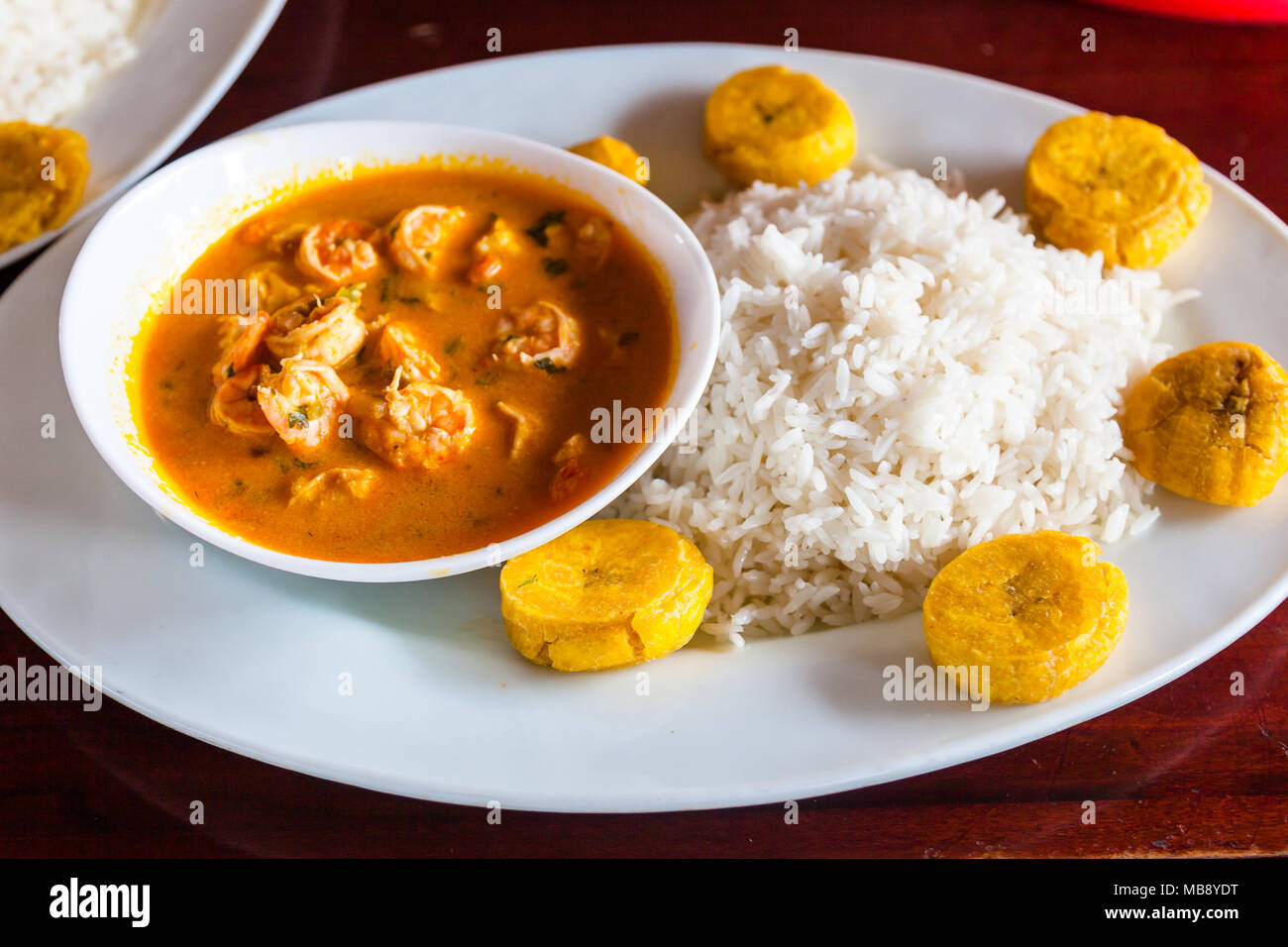 Coconut Shrimps Eintopf (encocado), in Weiß Teller serviert, mit Reis und gebratenen Bananen Stockfoto