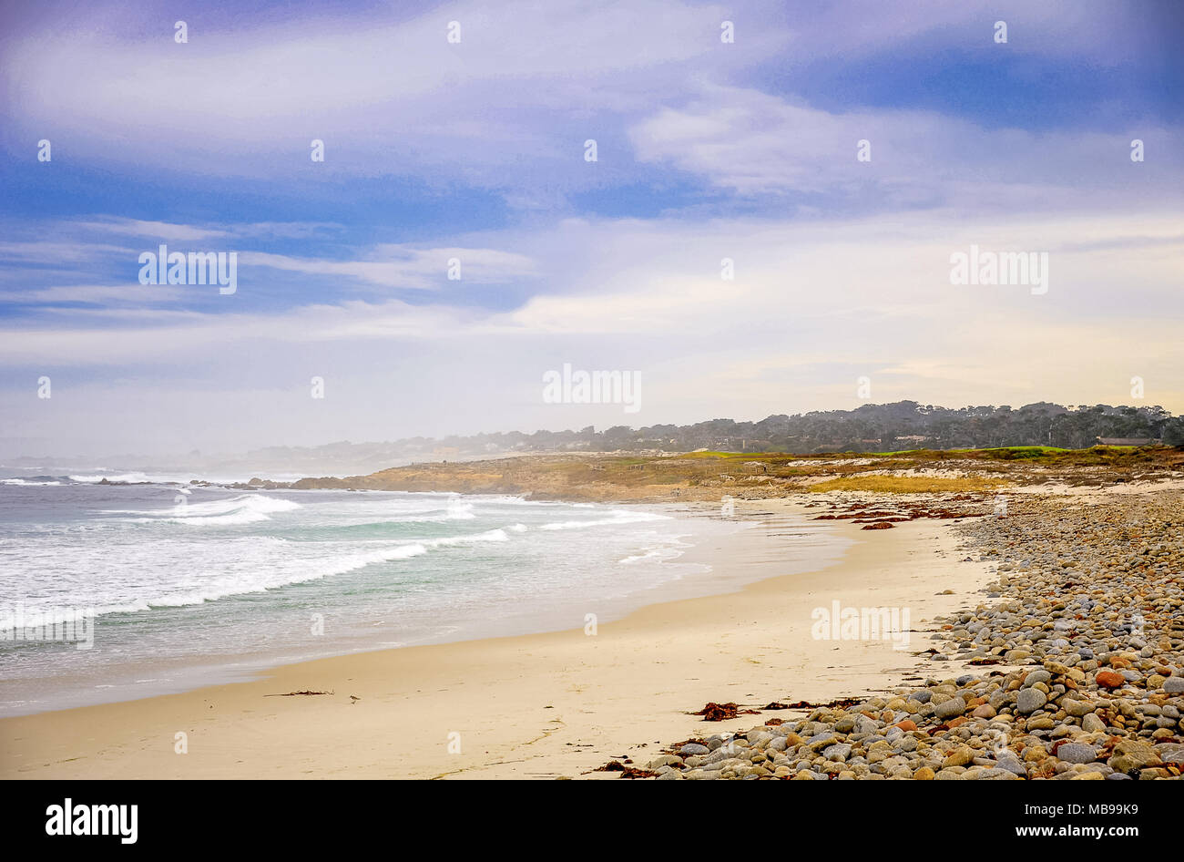 Pacific Ocean Marine in Pebble Beach in der Nähe von Monterey, Kalifornien. Schleier, Wellen, Sandstrand, farbige Felsen und Blau, bewölkter Himmel Stockfoto