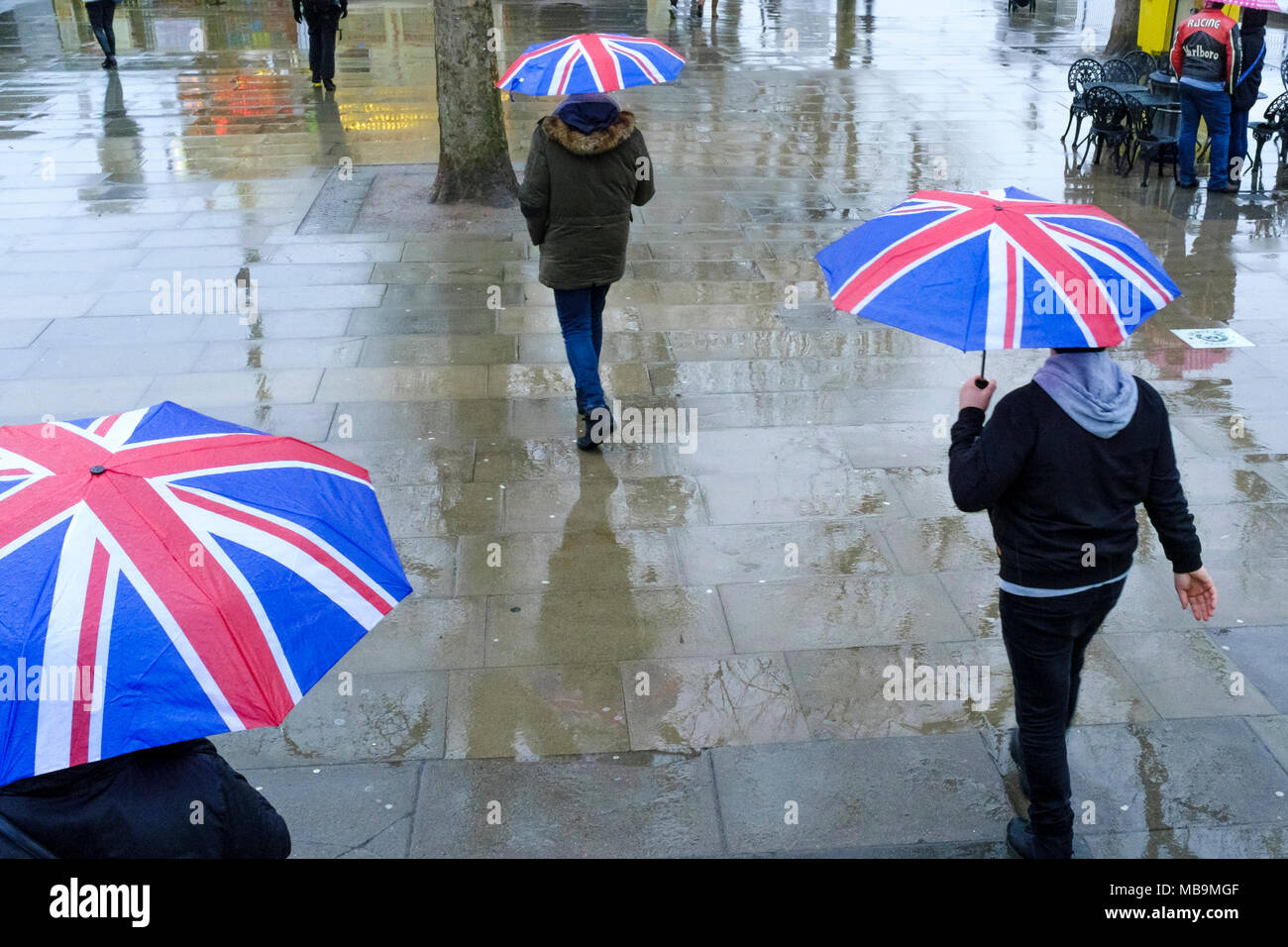 Fußgänger, die im Regen mit den Regenschirmen von Union Jack laufen, London, Großbritannien Stockfoto