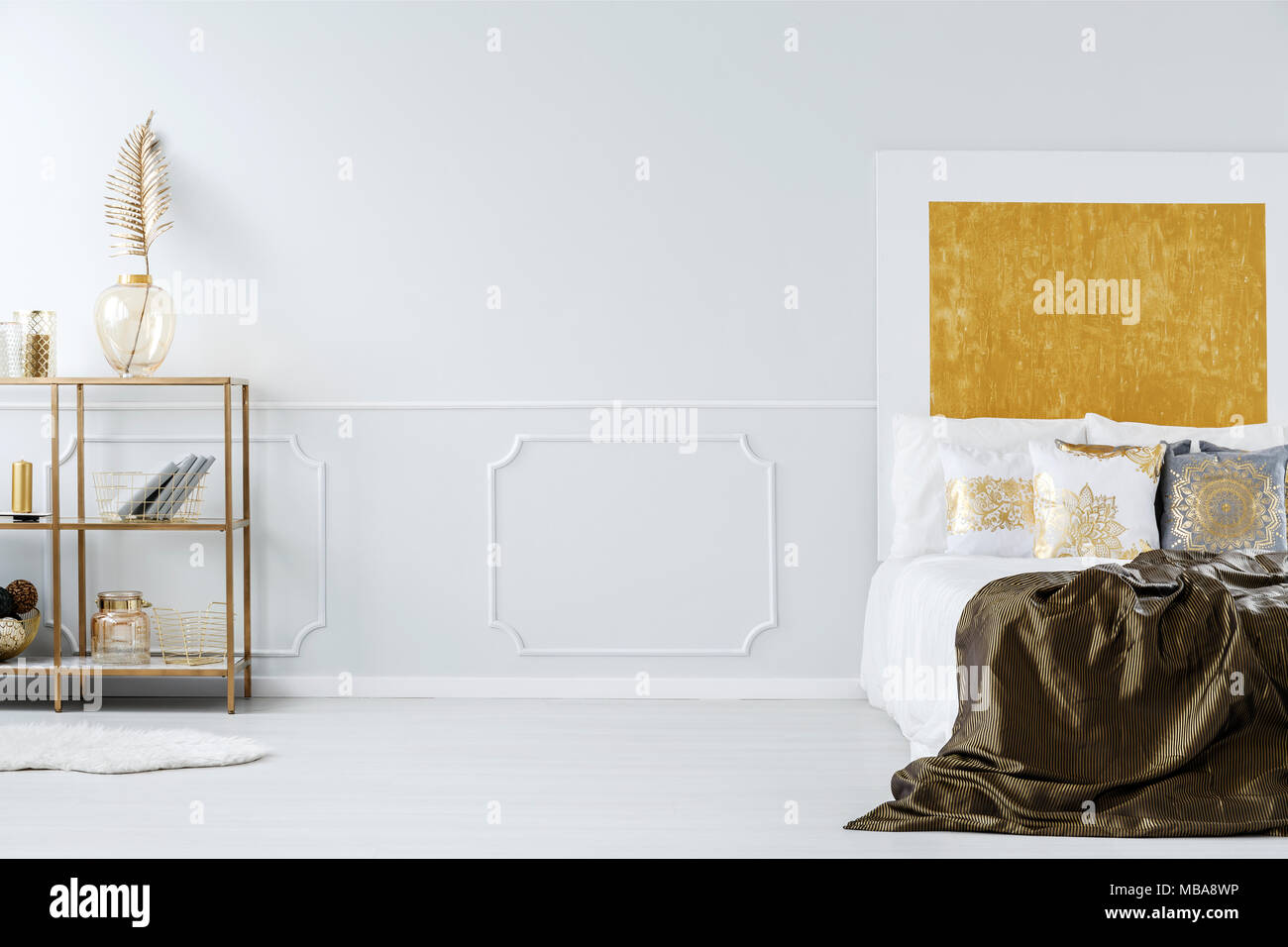 Kingsize-bett, leere Wand und Golden Regal mit Dekorationen im Schlafzimmer Innenraum Stockfoto