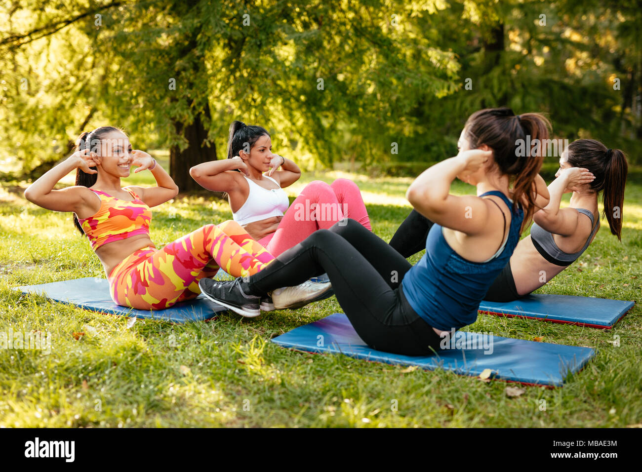 Vier schöne motivierte weibliche Freunde tun, Sit-up im Stadtpark. Stockfoto