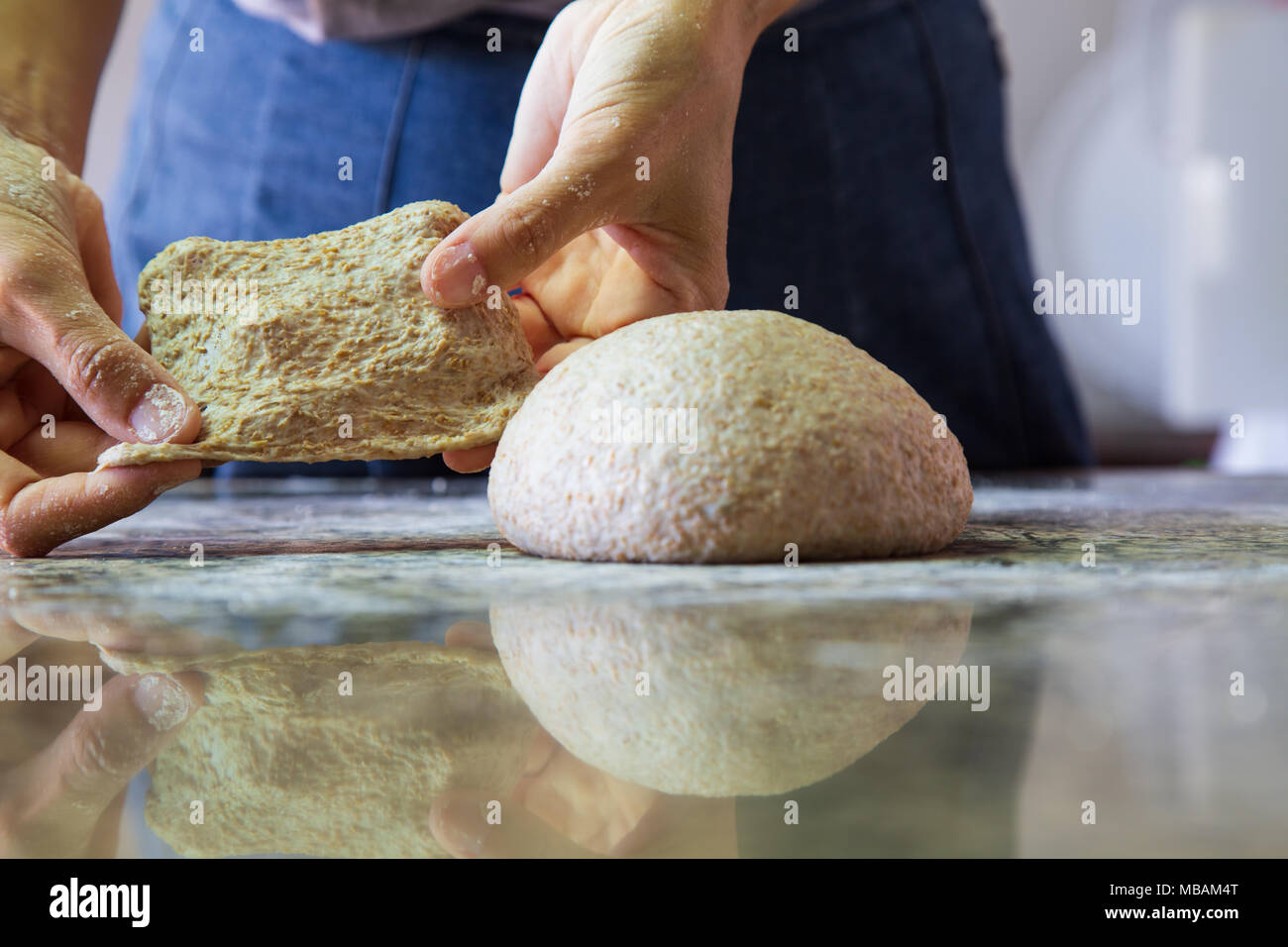 Weibliche Hände streckt den Teig, aus gemeinsamen Mehl und Vollkornmehl, mit Reflexion auf Granit Tisch, Bäckerei Sequenz Stockfoto