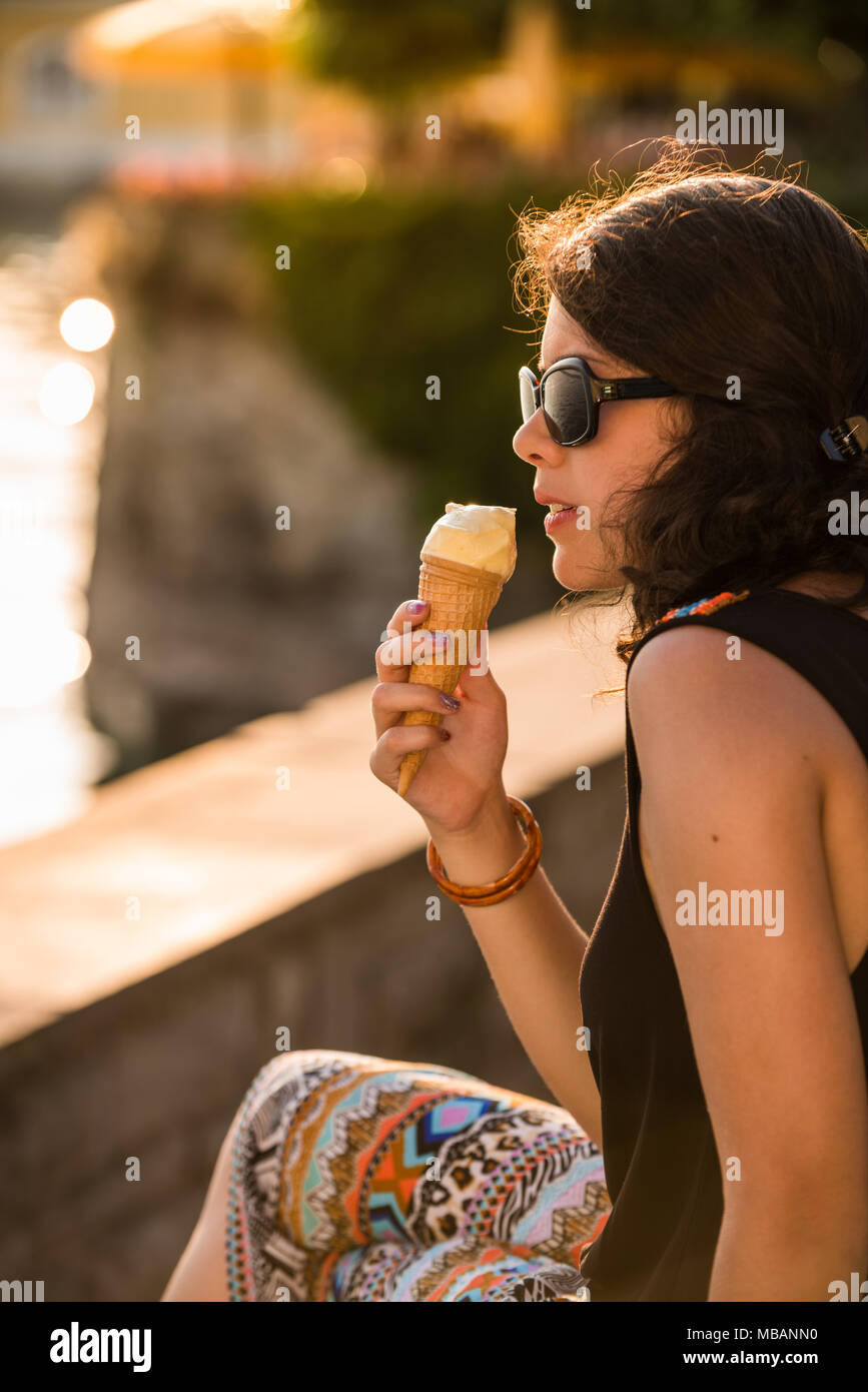 Junge und attraktive Frau essen Eis am See bei Sonnenuntergang Sonnenbrille tragen Stockfoto