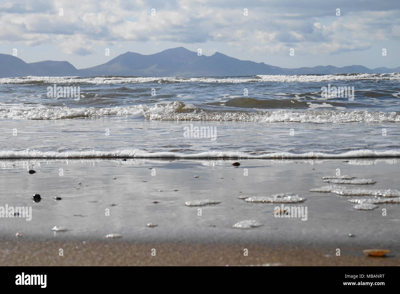 Schöne transparente Wasser an der Küste mit walisischen Berge, die sich aus den Horizont. In Anglesey in Whitby Strand (Niwbwrch). Stockfoto