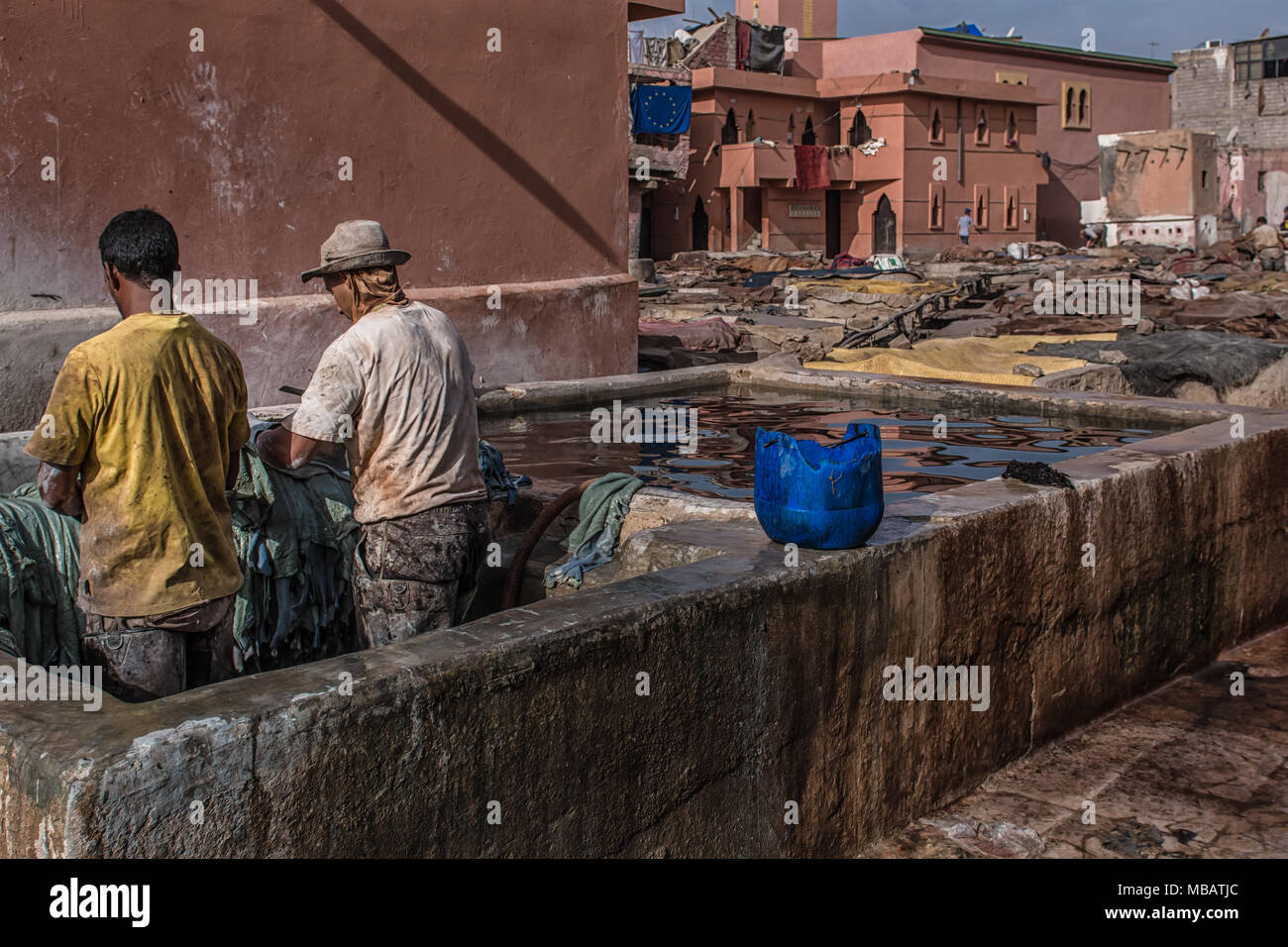 Zwei marokkanische Männer arbeiten in der marrakesch Gerberei Leder behandeln. Eine Grube der Farbstoff wird auf der rechten Seite. Das Leder ist in der Mwst.-chemischer Färbung getränkt. Stockfoto