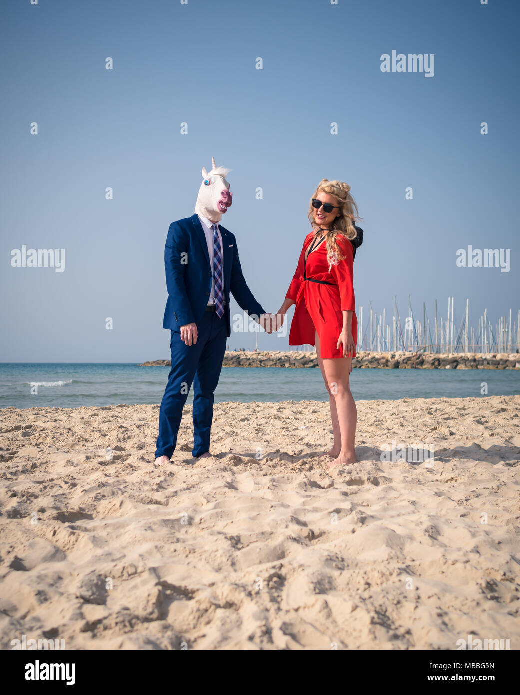 Ungewöhnliche Paare haben Ehe am Strand. Elegante Mann lustig Pferd Maske und Kostüm mit netten jungen Frau im roten Kleid Stockfoto