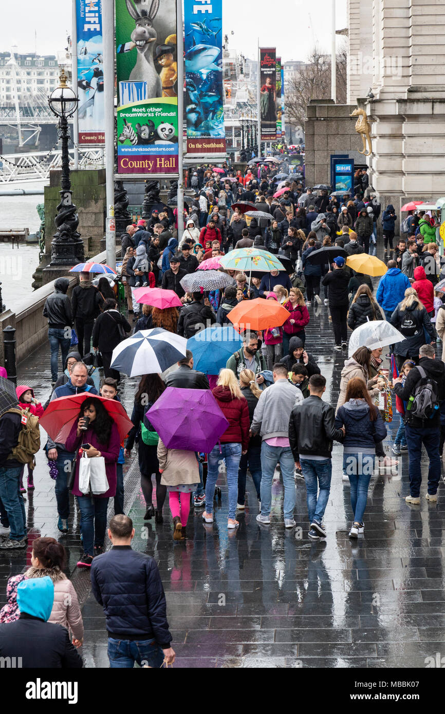 Touristen am Südufer der Themse in London, England. Wandern im Regen und viele Zuflucht unter Sonnenschirmen. Stockfoto