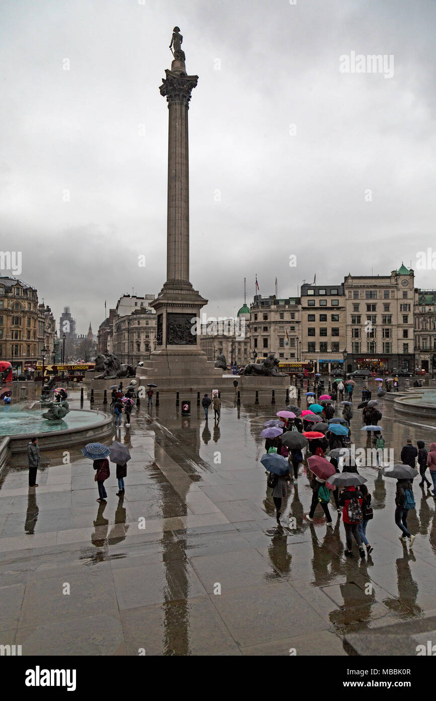 Touristen auf dem Trafalgar Square in London, Unterschlupf vor dem Regen unter Sonnenschirmen. Nelsons Column im Hintergrund. Stockfoto