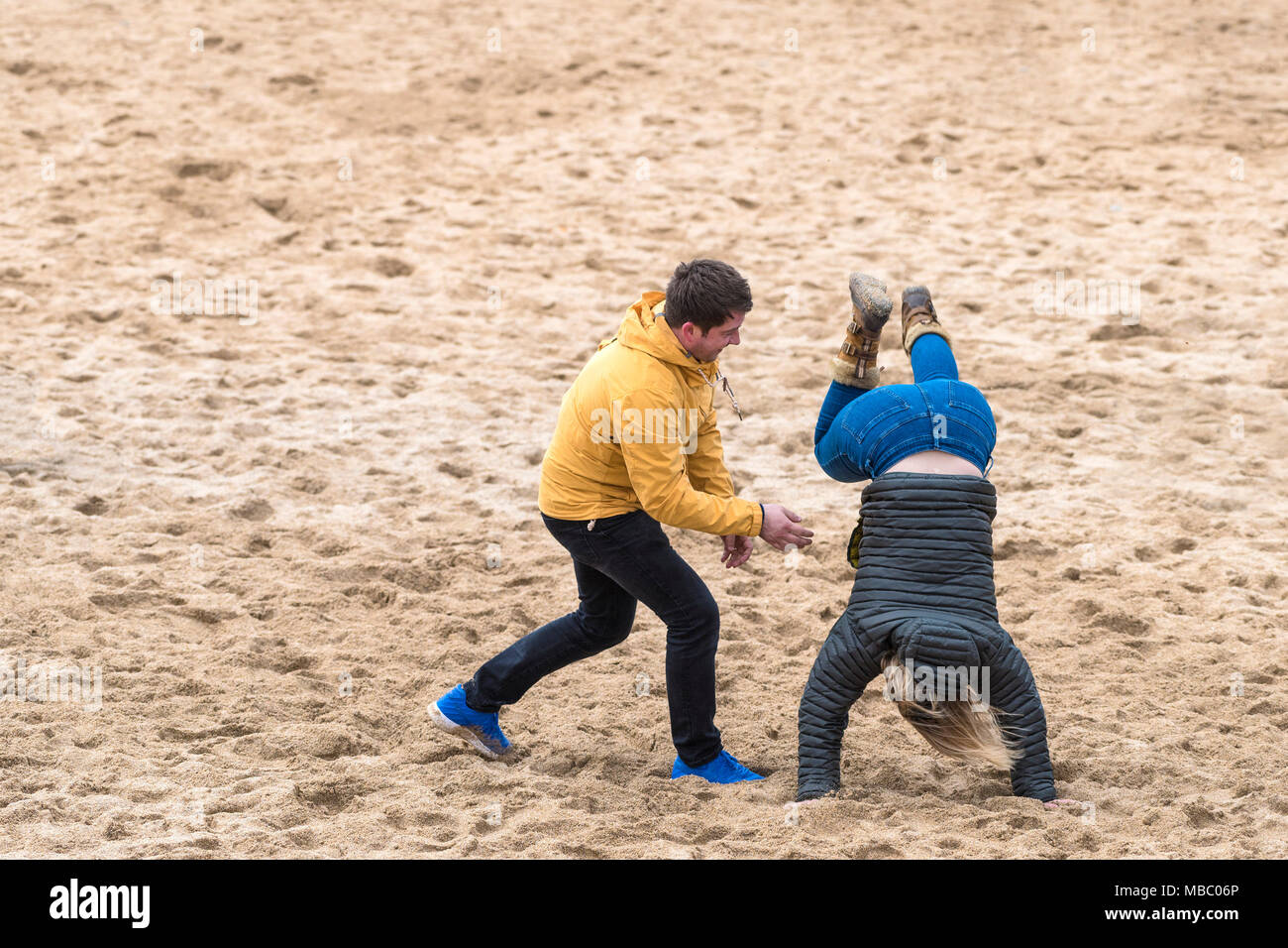 Ein Mann versucht zu helfen, seine Frau einen Handstand auf einem Strand durchführen. Stockfoto