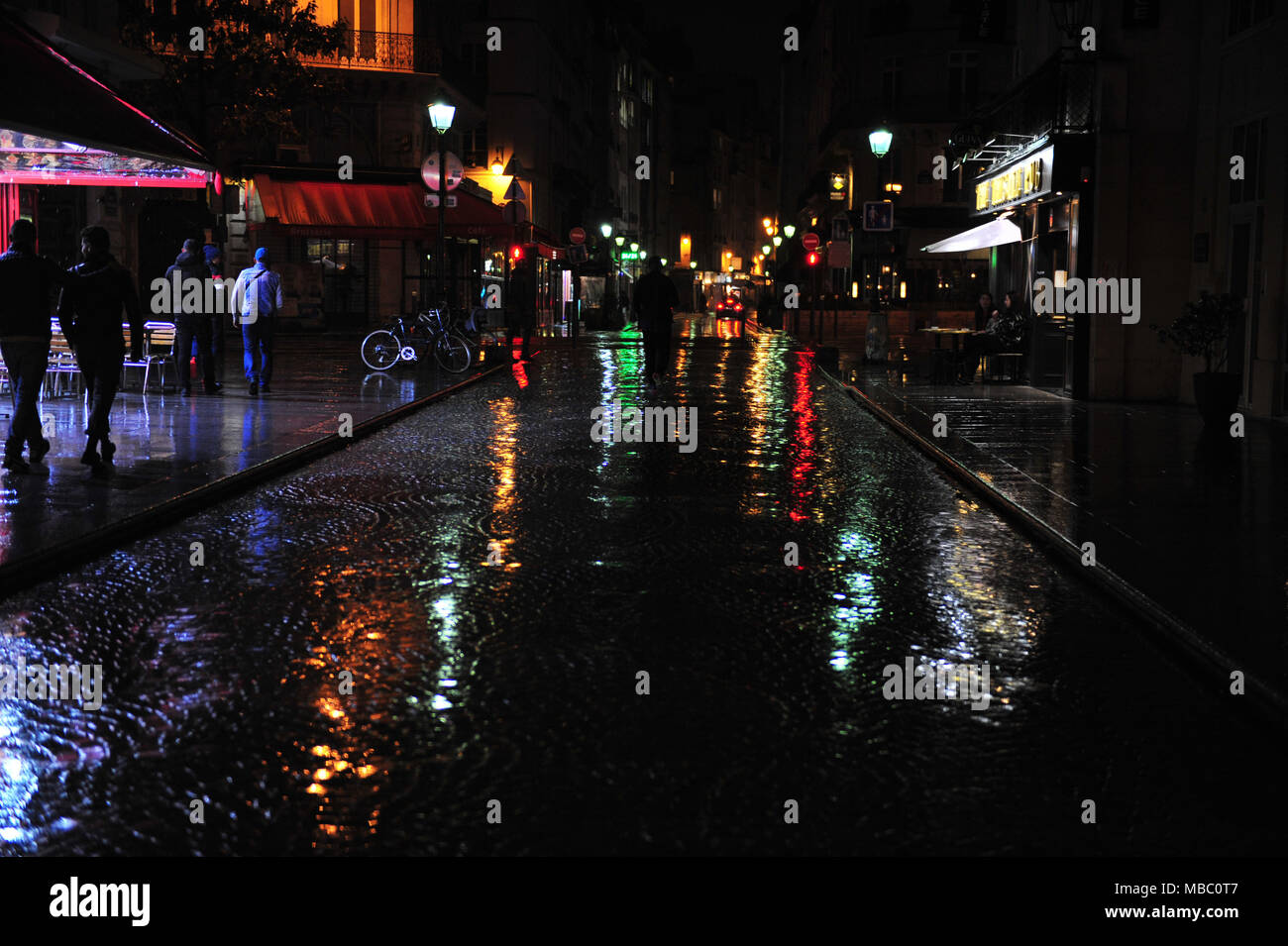 Stadt Straße in Paris an einem regnerischen dunklen Abend. Night Shot vom Restaurant Straße mit bunten Reflexionen über Kopfsteinpflaster. Nasse Oberfläche mit Farbe Stockfoto