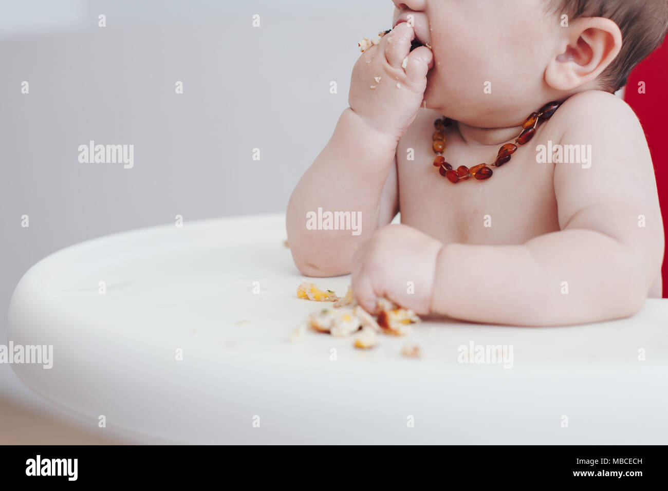 Schließen Ernte von 6 Monate alten Baby Junge selbst Fütterung in einem Hochstuhl Stockfoto