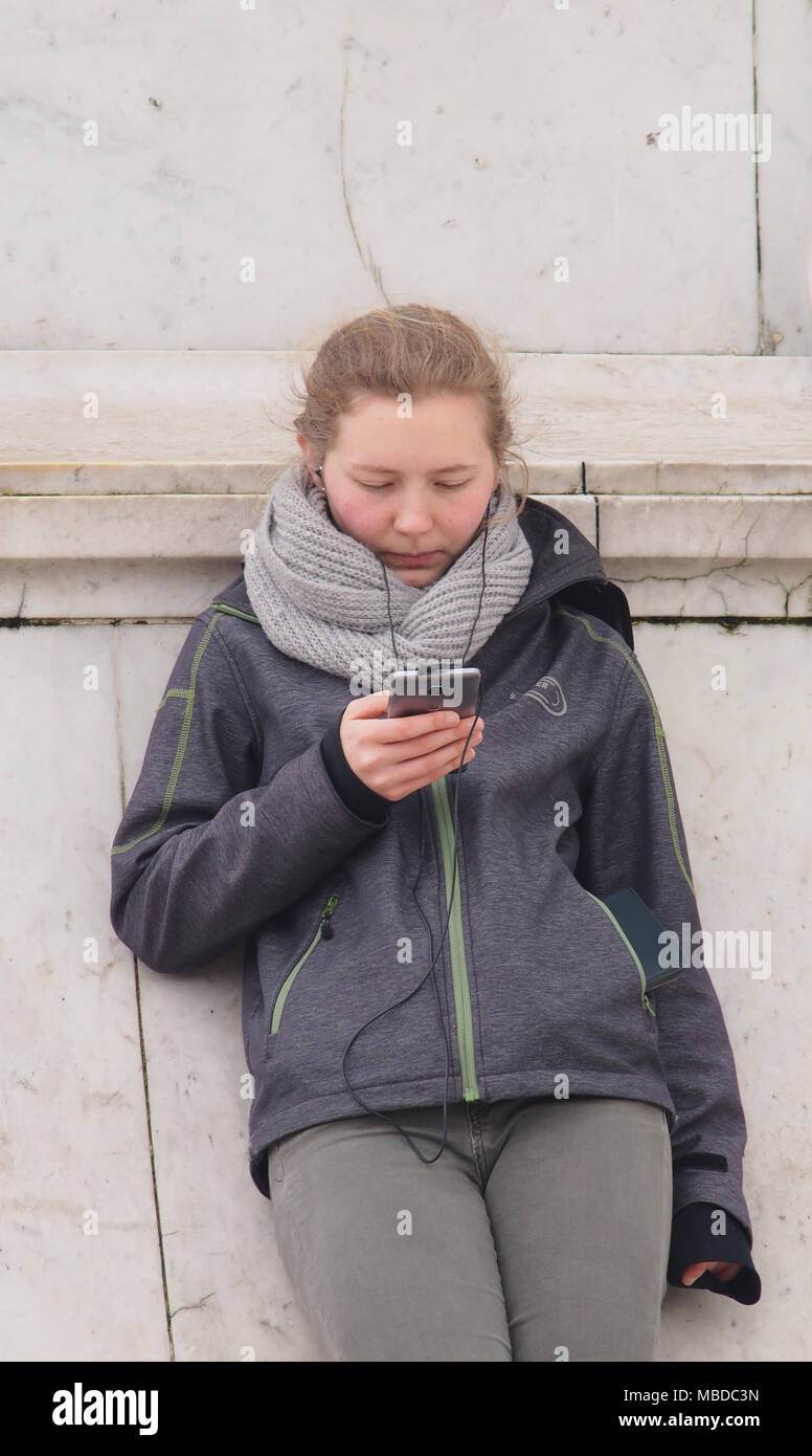 Eine junge Frau, die sich gegen die Königin Victoria statue Unterstützung vor dem Buckingham Palace, London, die auf Ihrem Smartphone Stockfoto