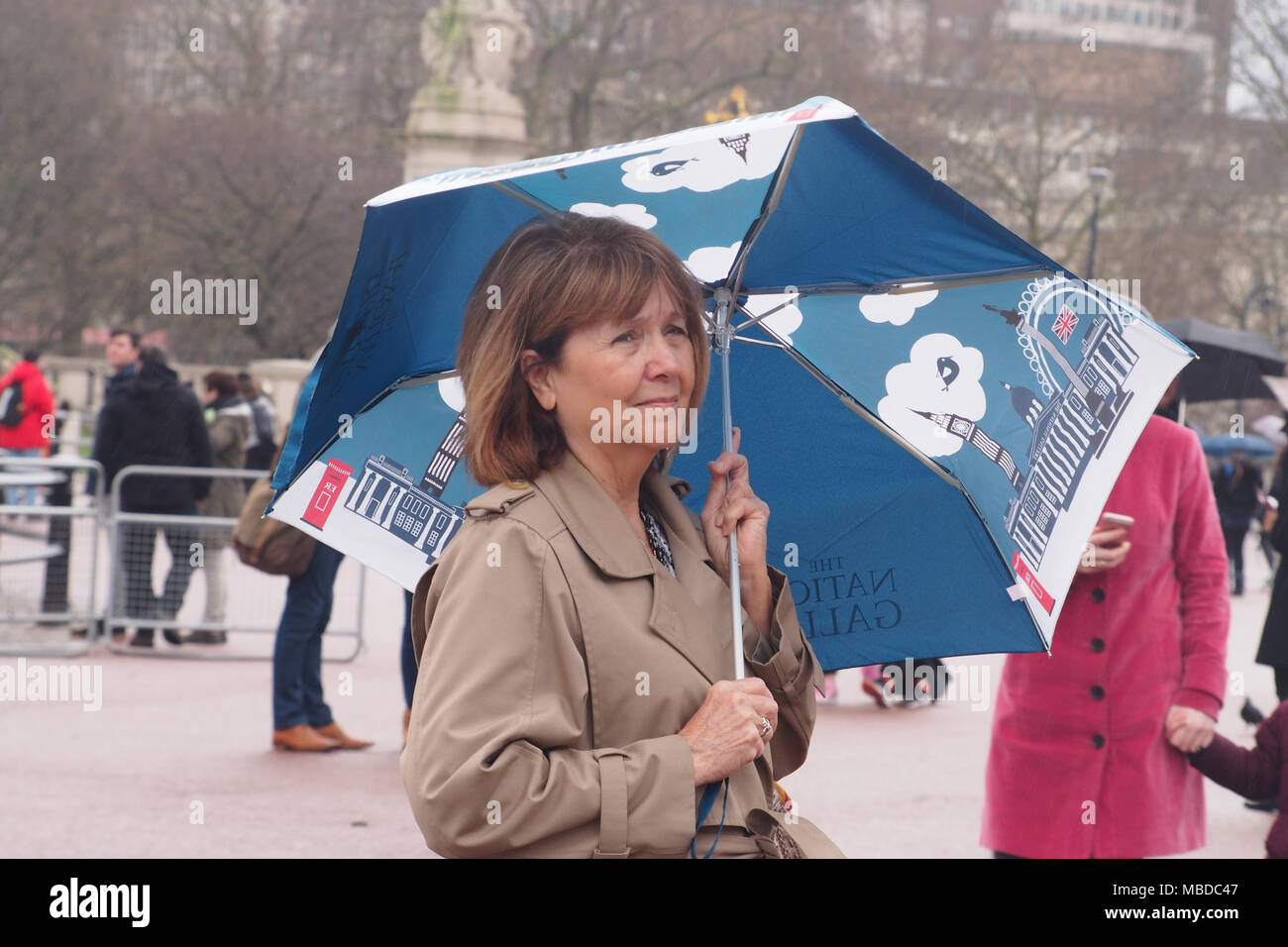 Eine Frau mittleren Alters im Rahmen eines Nationalen Galerie Regenschirm in den Bereich vor dem Buckingham Palace London Stockfoto