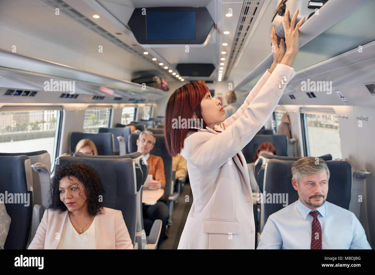 Geschäftsfrau verstauen Koffer in overhead Fach auf Personenzug Stockfoto