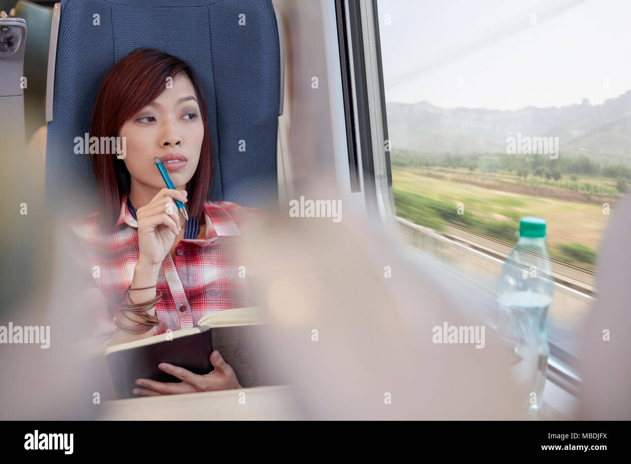 Nachdenkliche junge Frau schreiben im Journal und Blick aus Fenster auf Personenzug Stockfoto