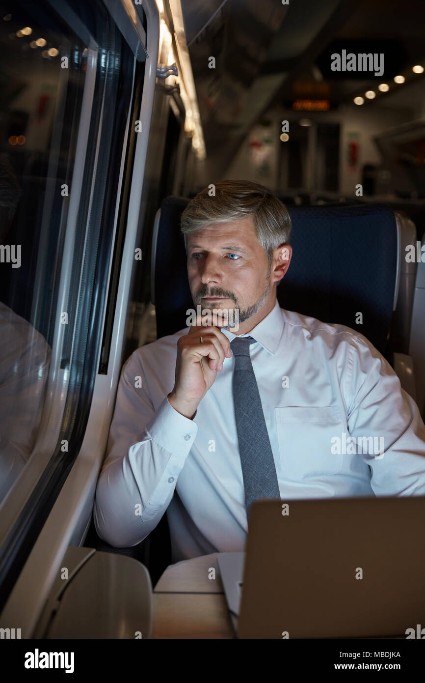 Ernsthafte, nachdenkliche Geschäftsmann am Laptop arbeiten, Fenster auf Personenzug in der Nacht Stockfoto