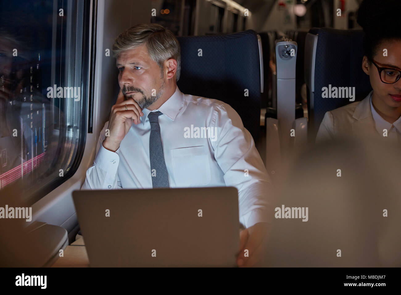 Ernsthafte, nachdenkliche Geschäftsmann am Laptop arbeiten, Fenster auf Personenzug in der Nacht Stockfoto