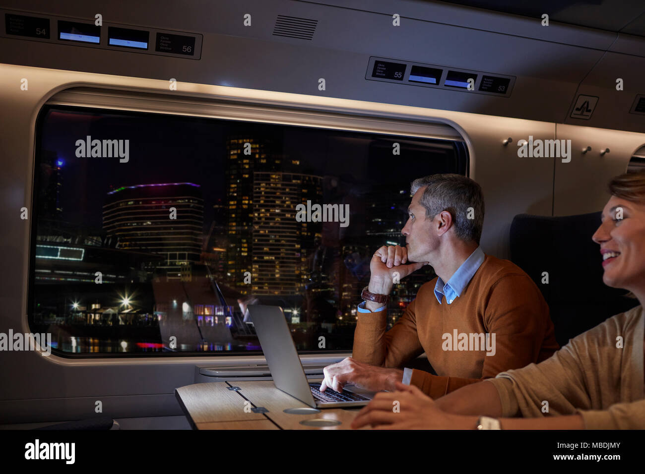 Unternehmer Arbeiten am Laptop auf Personenzug in der Nacht, mit Blick auf die Stadt Stockfoto