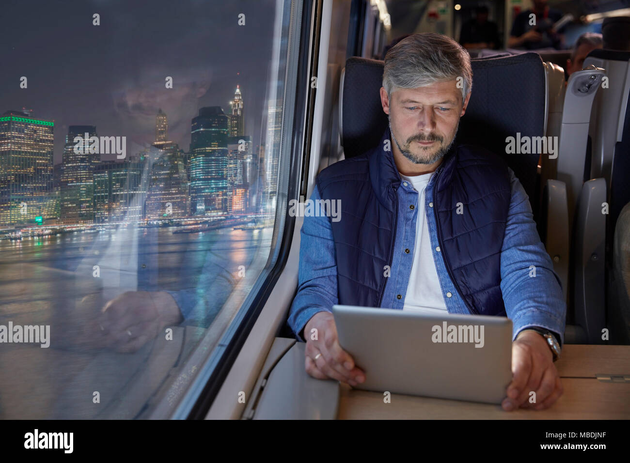 Mann mit digitalen Tablette auf Personenzug in der Nacht Stockfoto