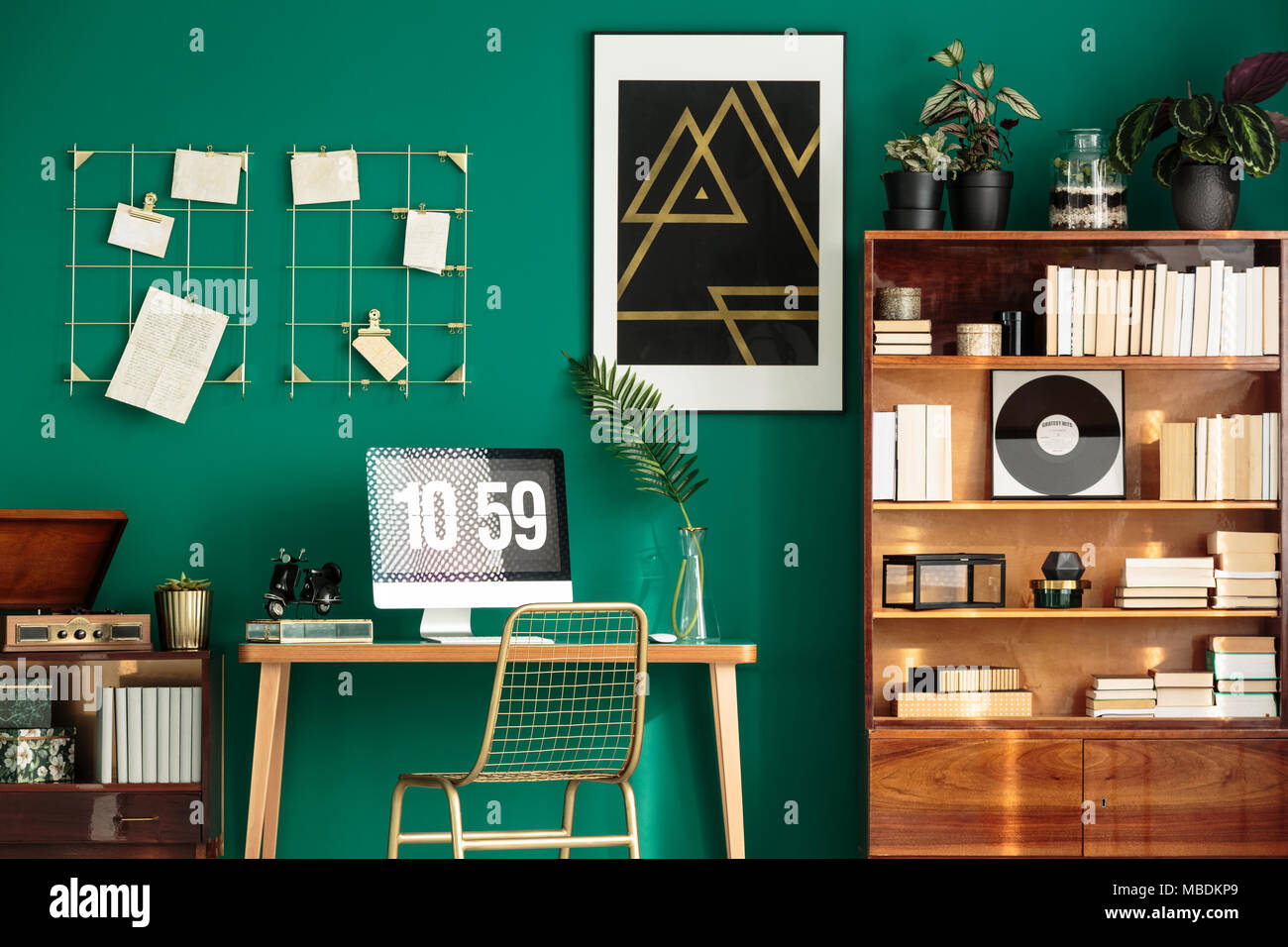 Monitor mit Uhr als Bildschirmschoner auf einem hölzernen Schreibtisch in grün Innenraum mit Büchern über zwei Schränke gelegt Stockfoto