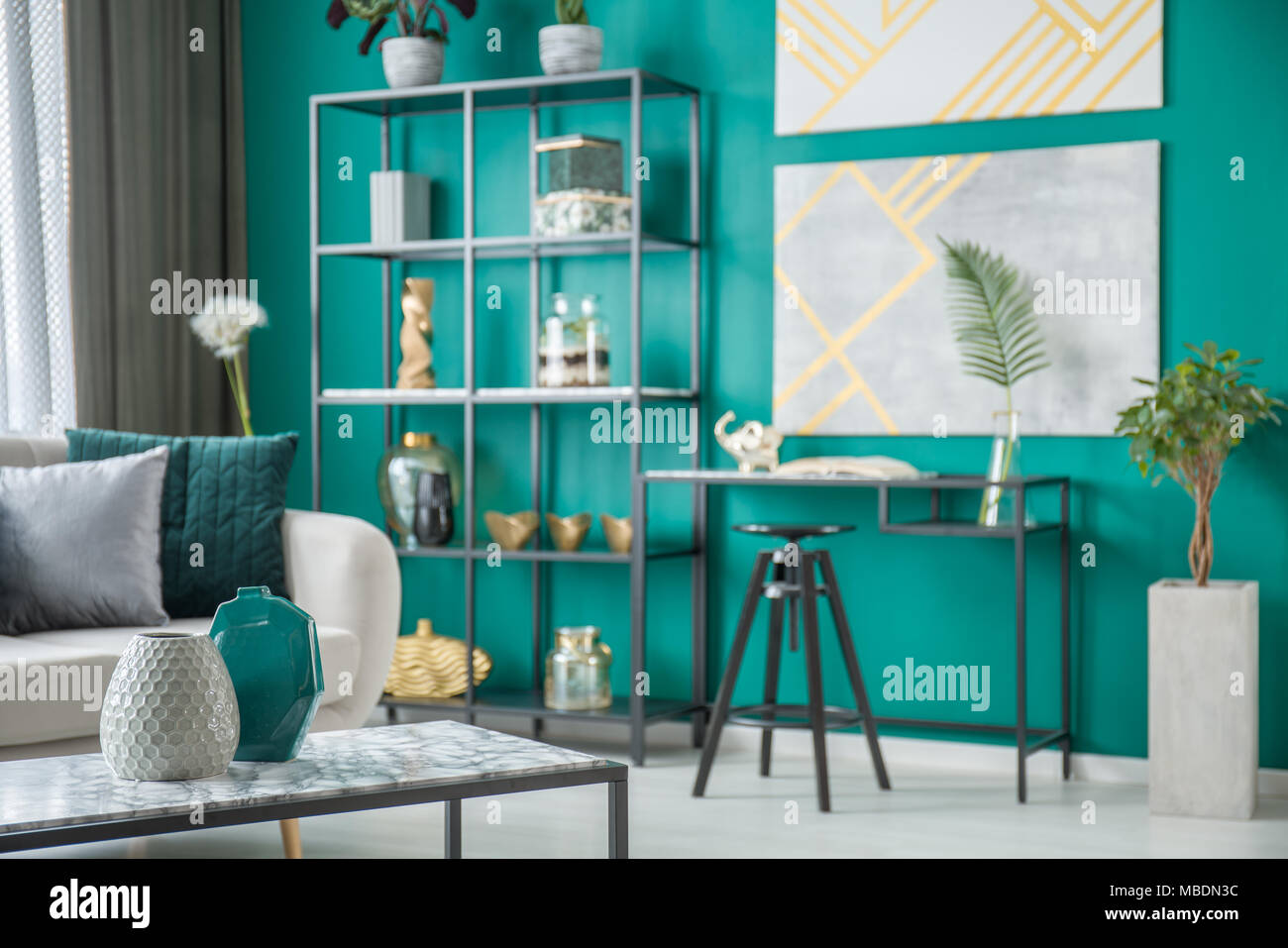 Schwarzer Stuhl am Schreibtisch gegen grüne Wand mit gold Poster im Wohnzimmer Interieur mit Vasen Stockfoto
