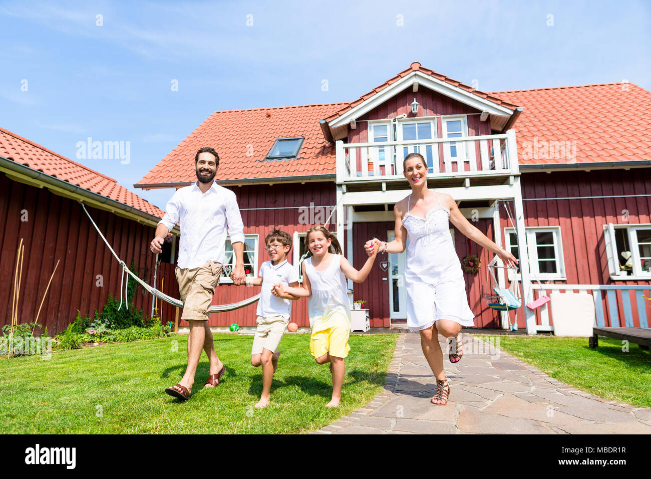 Glückliche Familie laufen auf der Wiese vor dem Haus Stockfoto