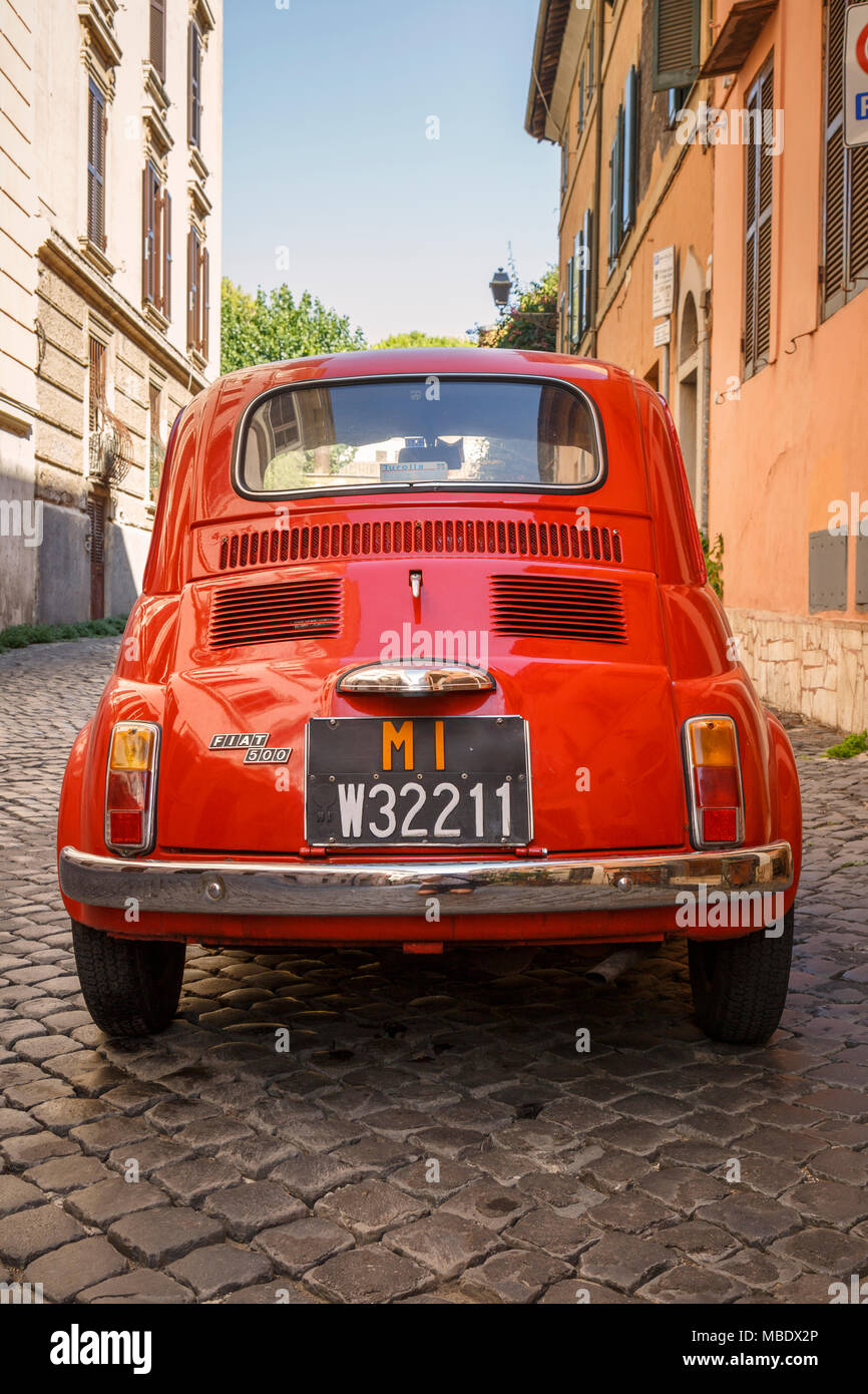 Rückansicht eines alten roten Fiat 500 in einer gepflasterten Straße in Rom, Italien, außerhalb eines Gebäudes unter italienischer Flagge geparkt. Die nummernschilder ein MI pr anzeigen Stockfoto